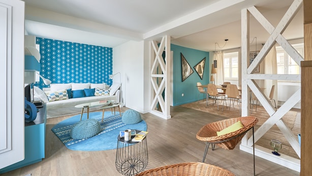 A spacious living area with a blue patterned wall, a white sofa, and a dining area with chairs and a table.