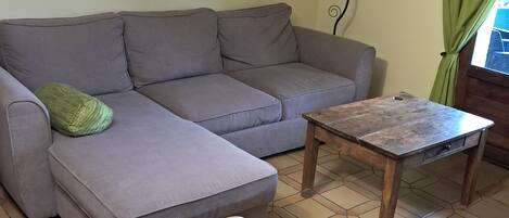 Una sala de estar con un sofá gris, una mesa de centro de madera y una silla de mimbre.