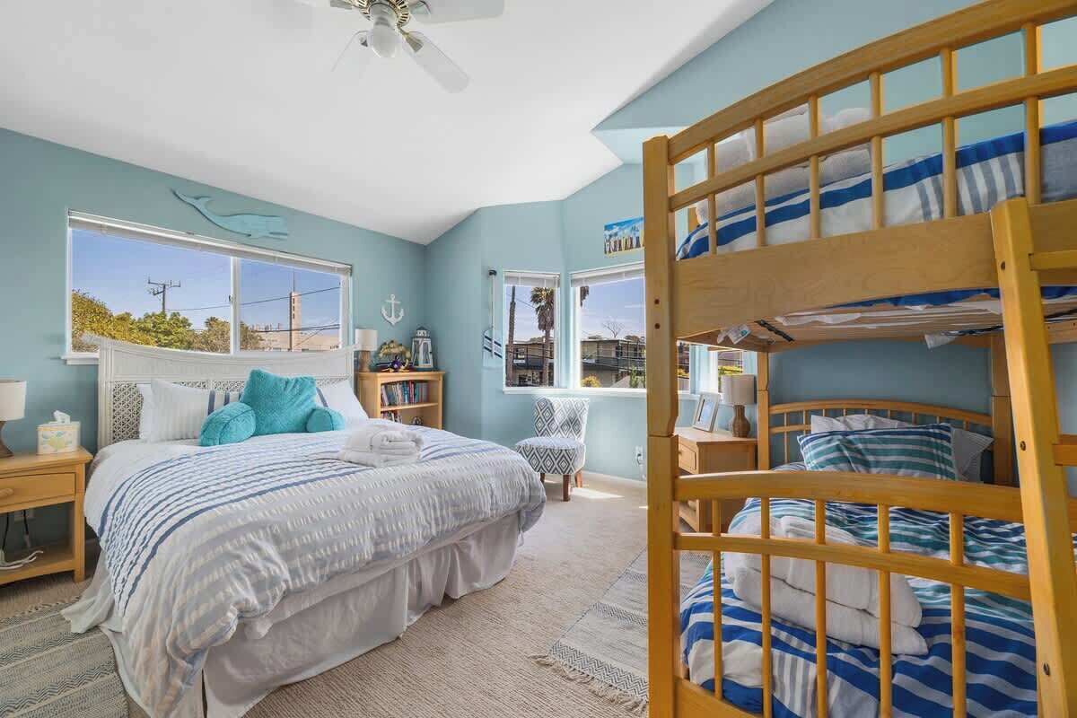 A bedroom with a bunk bed, a large window, a desk, and a chair.