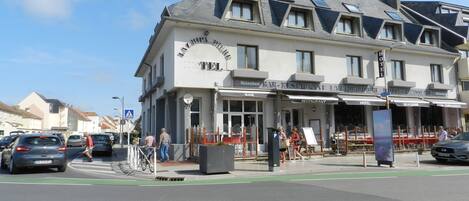 Et hotel med bar og restaurant i stueetagen, flere vinduer og en parkeringsplads.