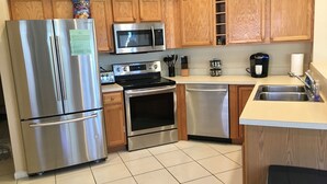 Una cocina moderna con electrodomésticos de acero inoxidable, armarios de madera y suelo de baldosas.