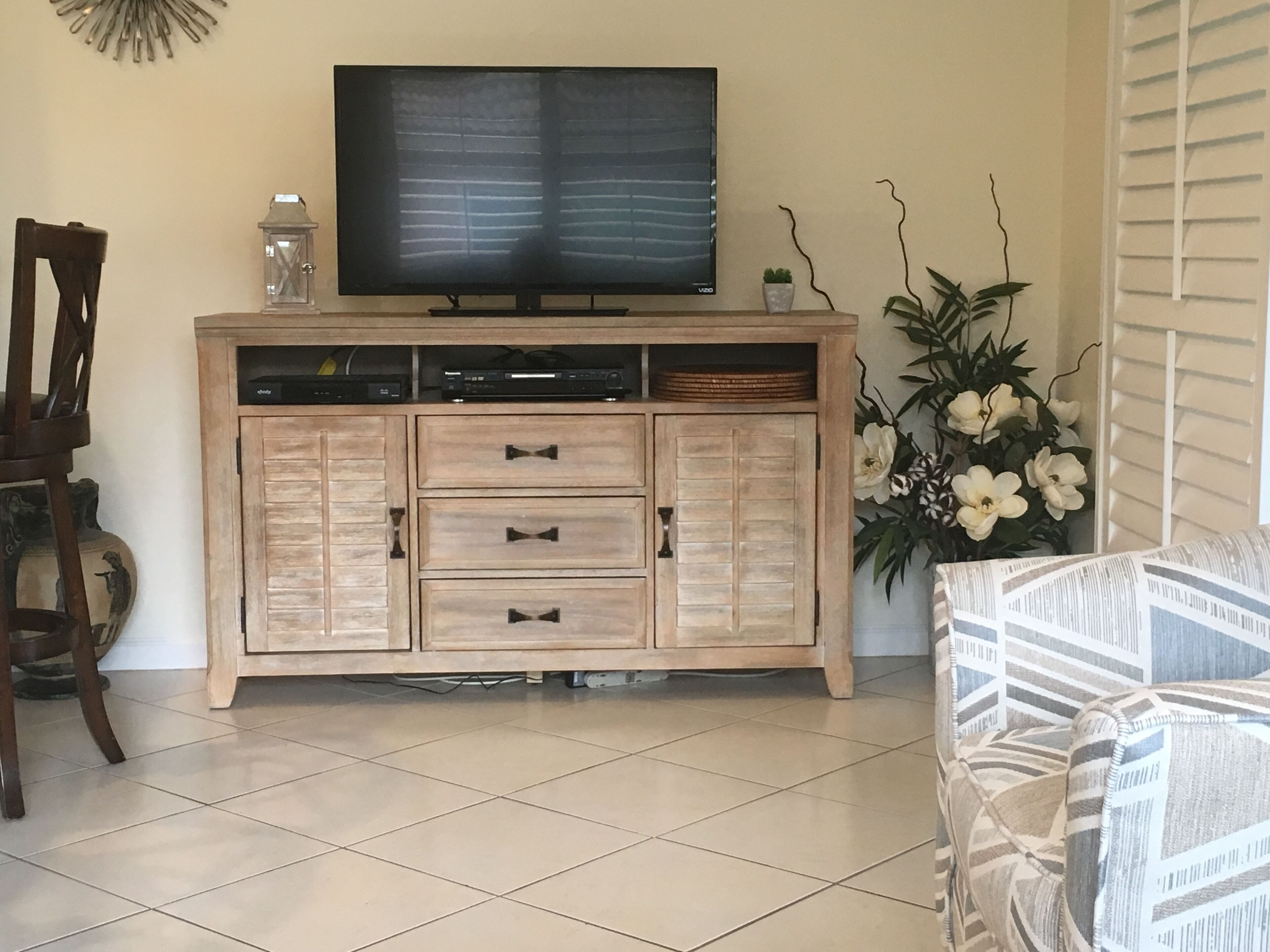 A living room with a wooden cabinet, a flat-screen TV, a decorative plant, and a patterned sofa.