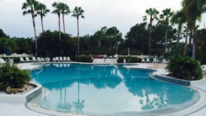 Una piscina de borde curvo, rodeada de sillas reclinables blancas y palmeras.