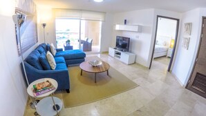 A living room with a sofa, coffee table, TV, and a small table with books. - RELAXING OCEAN VIEW CONDO (Oranjestad West)