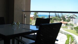 A balcony with a glass table and wicker chairs, overlooking a residential area with houses and a clear sky. - RELAXING OCEAN VIEW CONDO (Oranjestad West)