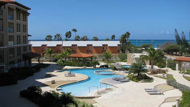A resort with a large pool area, multiple lounge chairs, and a view of the ocean. - RELAXING OCEAN VIEW CONDO (Oranjestad West)
