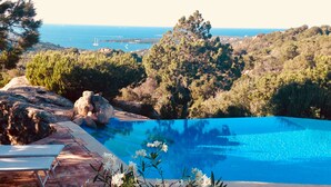 Una piscina de agua cristalina y azul, rodeada de rocas y árboles, con vistas a un paisaje costero.