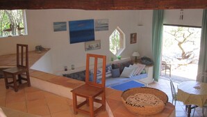 Un cuarto acogedor con techo de madera, un sofá con cojines, una mesita y un ventanal con vistas a árboles.