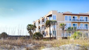 Un hôtel situé en bord de mer, doté de nombreux balcons et donnant sur une plage de sable.
