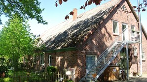A brick building with a steeply pitched roof, a wooden staircase leading to a balcony, and a small garden area with various plants and a birdhouse. - Holiday in the Elbe Weser triangle on a Resthof near the North Sea (Hipstedt)