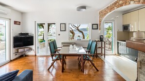 A spacious living area with a wooden dining table, teal chairs, a flat-screen TV, and a stone accent wall. - Villa near Trogir - private beach, bbq, parking, turqouise sea, boat rental :) (Rogoznica)