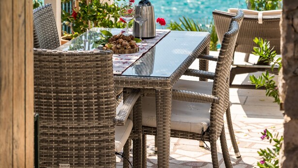 An outdoor dining area with wicker furniture, a glass table, and a view of the sea through an archway. - Villa near Trogir - private beach, bbq, parking, turqouise sea, boat rental :) (Rogoznica)