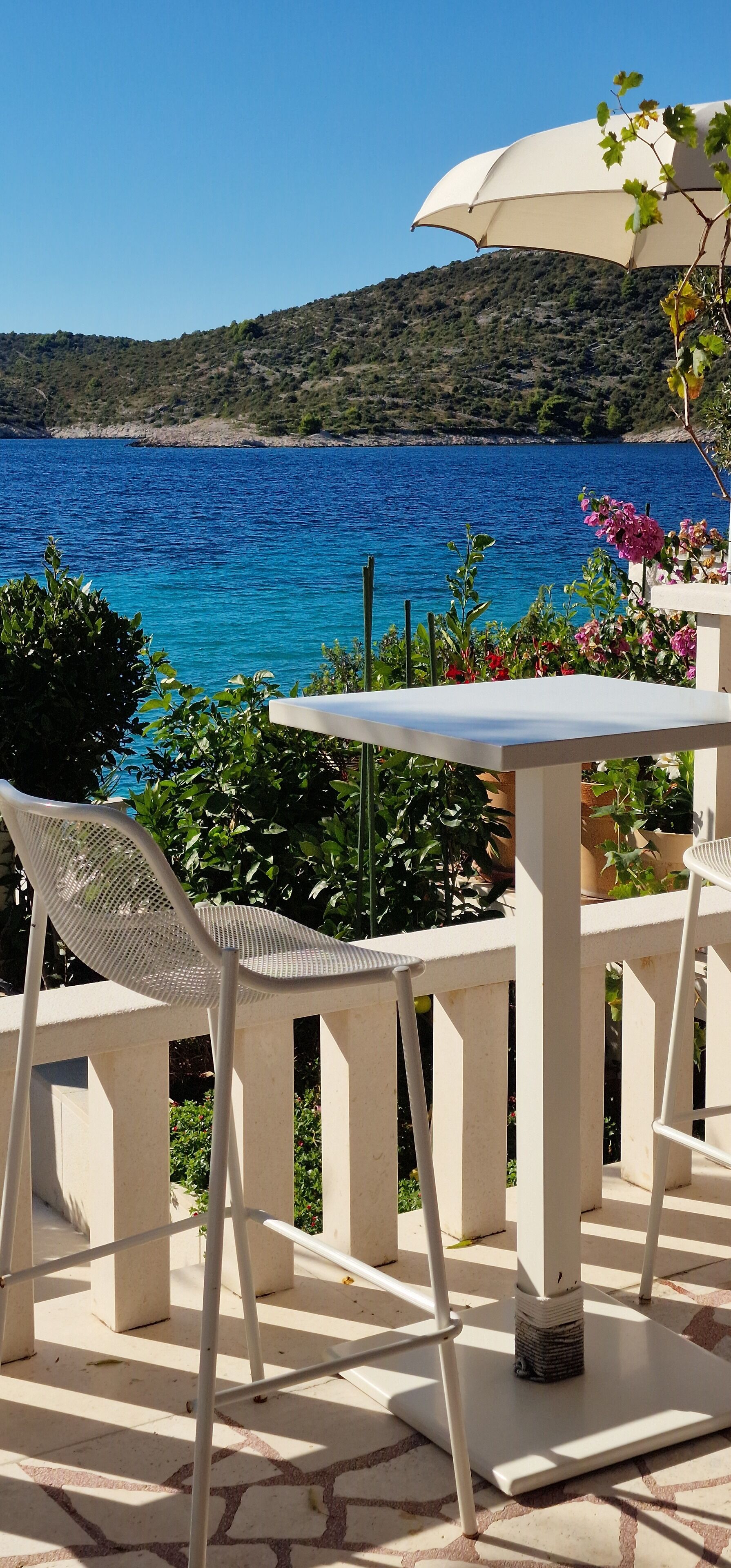 A table and chairs set outdoors with a view of a blue sea and a hilly landscape.