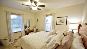 A bedroom with a bed, a desk, a chair, a ceiling fan, and a window.