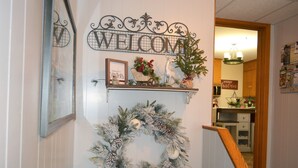A decorated entryway with a 'WELCOME' sign, a Christmas wreath, and a 'Merry Christmas' sign.