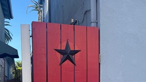 A red gate with a black star emblem, a white pillar, and a blue building in the background. - Small Private Apartment Within Walking Distance to Beach, Restaurants & Shops (Corona del Mar)