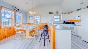 A spacious kitchen with a central island, wooden dining area, and large windows. - Oceanview Home with Private Pool, Hot Tub, and Nearby Community Beach Access (Rodanthe)