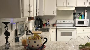 Une cuisine avec des meubles blancs, un four à micro-ondes, une cuisinière et une machine à café.