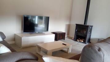 Ein modernes Wohnzimmer mit Fernseher auf einer weißen Konsole, einem kleinen Holztisch und einem Kamin.