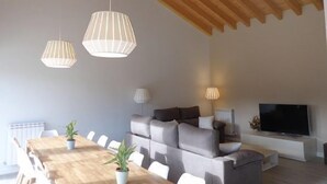 Ett modernt vardagsrum med ett träpanelat tak, en soffgrupp, en tv och en matplats med bord och stolar.
