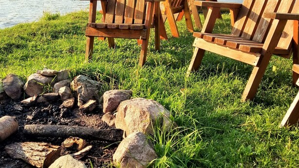 Dos sillas Adirondack de madera junto a un lago, con un brasero al frente.
