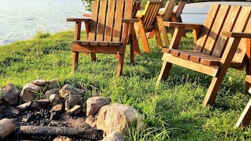 Deux fauteuils Adirondack en bois, placés au bord d’un lac, avec un foyer au premier plan.