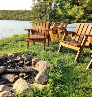 Deux fauteuils Adirondack en bois, placés au bord d’un lac, avec un foyer au premier plan.