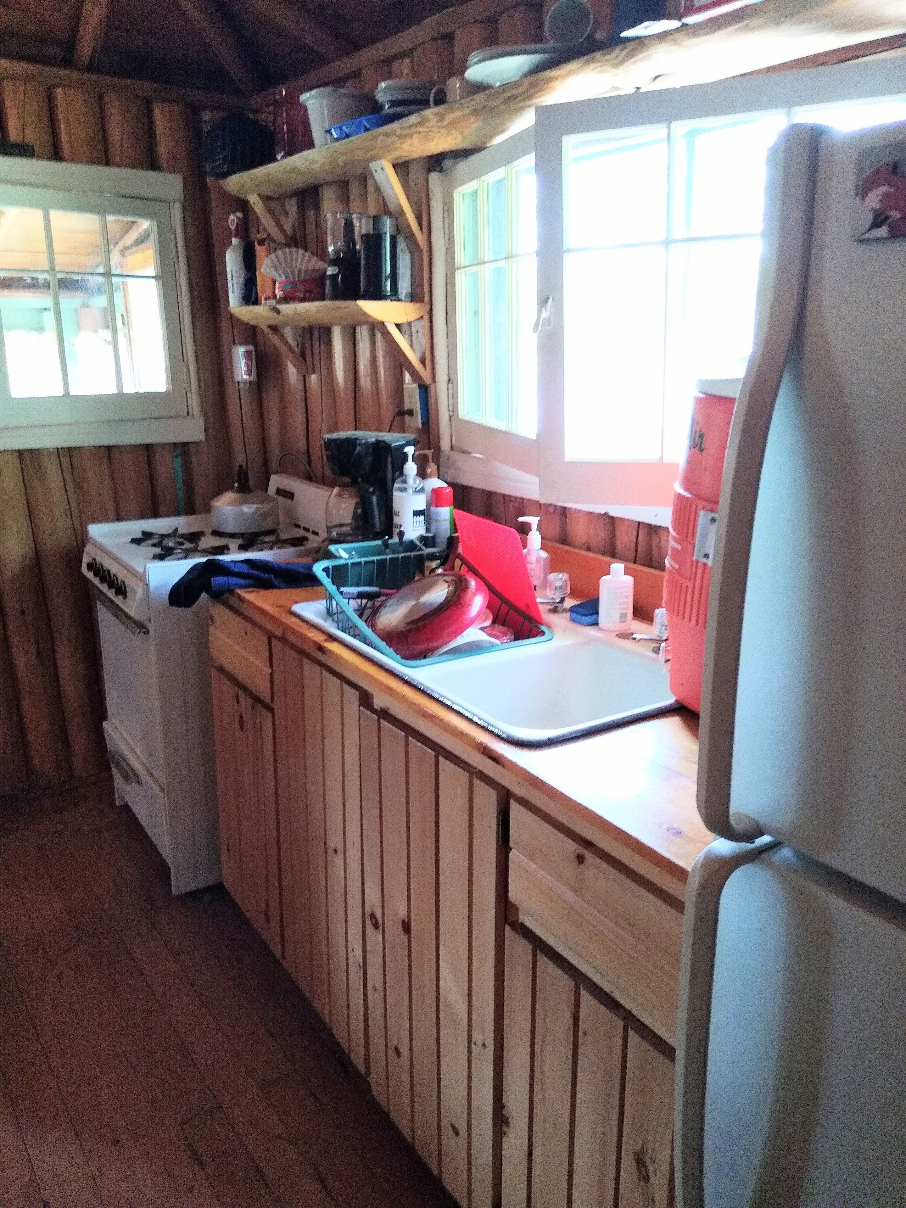 Une cuisine rustique aménagée dans une cabane en bois, avec un poêle, un évier et un réfrigérateur.