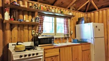 A kitchen with wooden cabinets, a stove, a microwave, a refrigerator, and shelves with various items.
