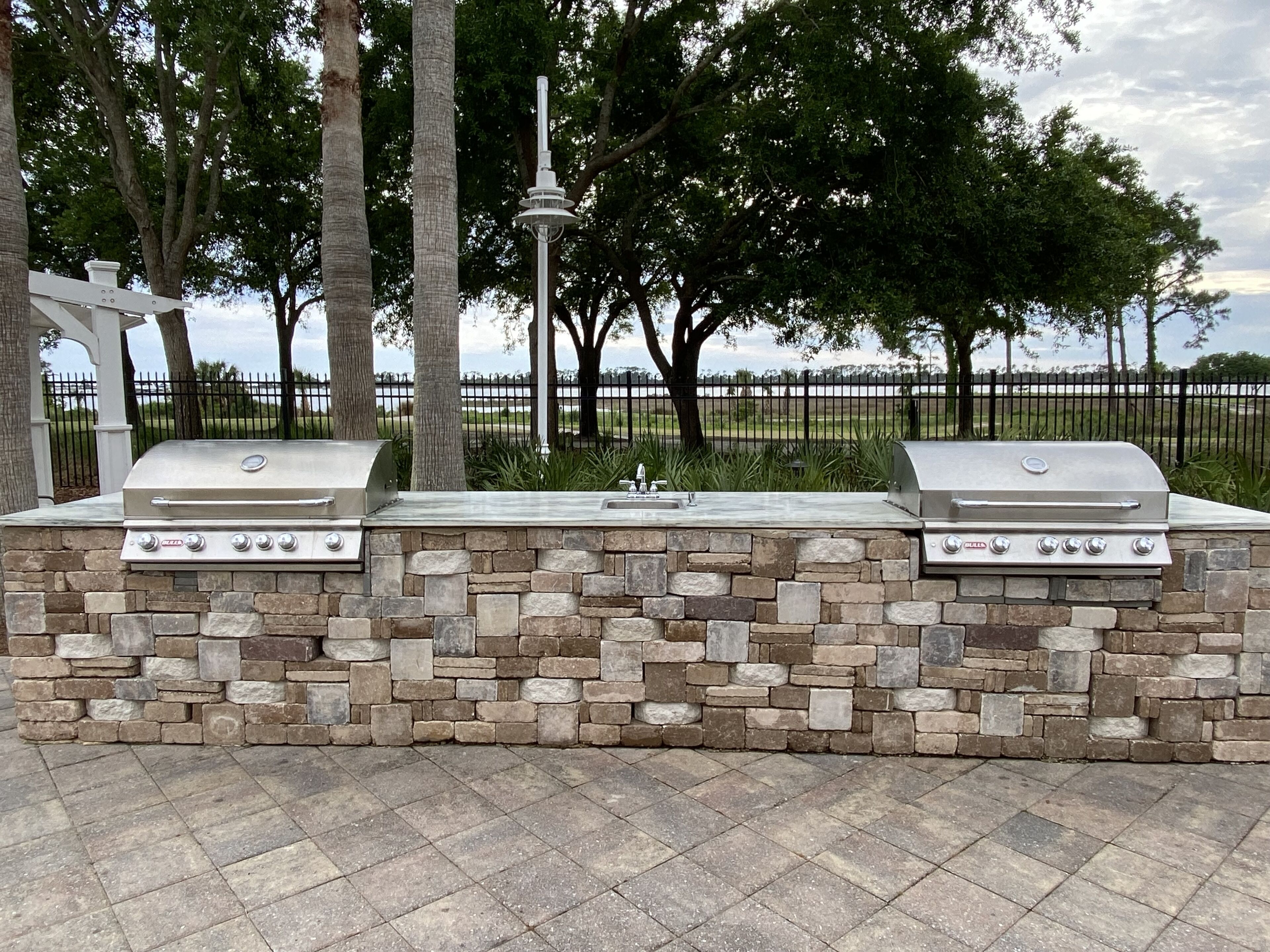 An outdoor grill station with two gas grills, a sink, and a stone wall.