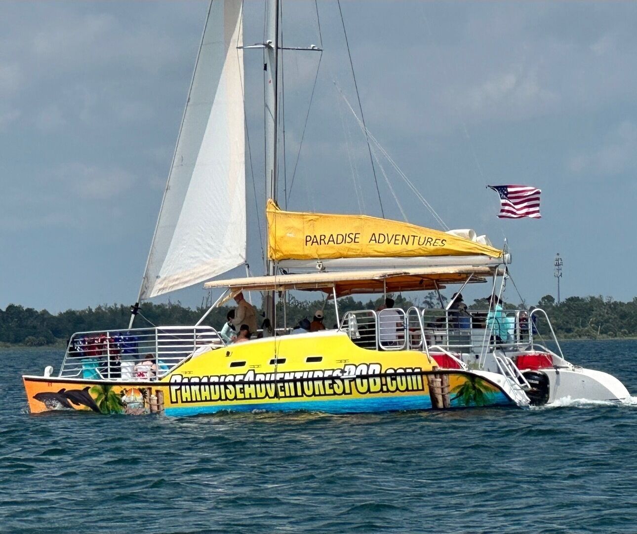 A colorful boat with a sail, a canopy, and an American flag, floating on water.