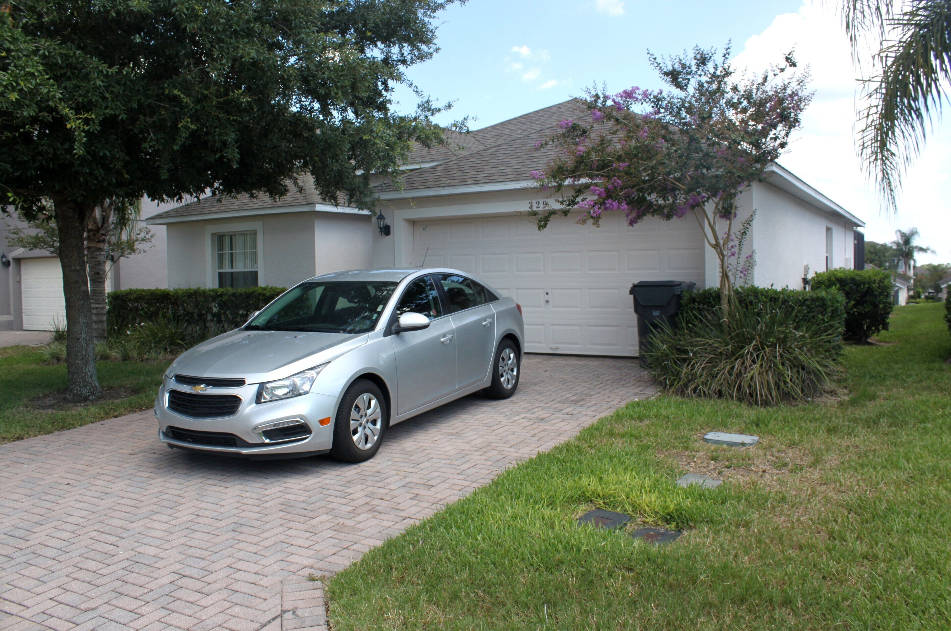 A silver car parked in front of a house with a garage.