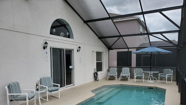 Ein Innenpool mit Glasdach, umgeben von weißen Stühlen und einem Tisch, sowie eine überdachte Terrasse mit Sonnenschirmen.