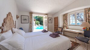 A bedroom with a bed, a chair, a window with curtains, a radiator, and a view of an outdoor swimming pool. - Villa panoramic sea view gulf of Saint -Tropez swimming pool 6 bedrooms 6 bathrooms 12 pers (Sainte-Maxime)