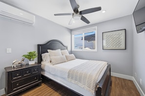 Un dormitorio con cama, cómoda, ventilador de techo, ventana y un cuadro en la pared.