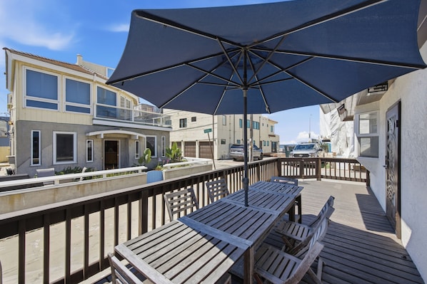 Una terraza de madera con un paraguas grande, asientos exteriores y vistas a una zona residencial.