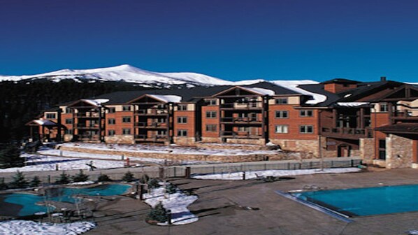 A multi-story hotel with a pool area, snow-covered ground, and a mountain in the background. - Grand Timber Lodge Ski in/Ski out --two bedroom (Breckenridge)