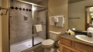 A bathroom with a glass-enclosed shower, a toilet, a sink with a mirror, and towels hanging on the wall. - Grand Timber Lodge Ski in/Ski out --two bedroom (Breckenridge)