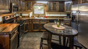 A rustic kitchen with wooden cabinets, a stainless steel refrigerator, a built-in oven, and a dining table with chairs.