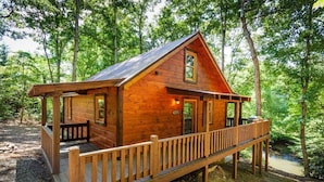 A wooden cabin with a porch, surrounded by trees.