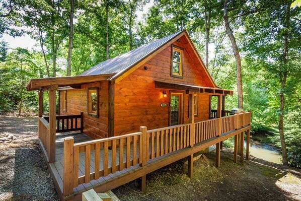 A wooden cabin with a porch, surrounded by trees.