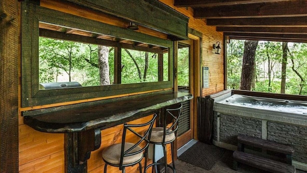 A wooden cabin with a bar area featuring two stools, a bench, and a hot tub.
