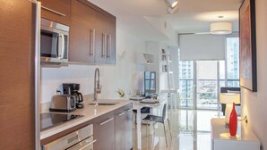 A modern kitchen with stainless steel appliances, a dining area with a glass table, and a view of the city through large windows.