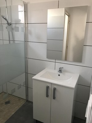 A bathroom with a glass shower enclosure, a white sink with a mirror above it, and a tiled floor.