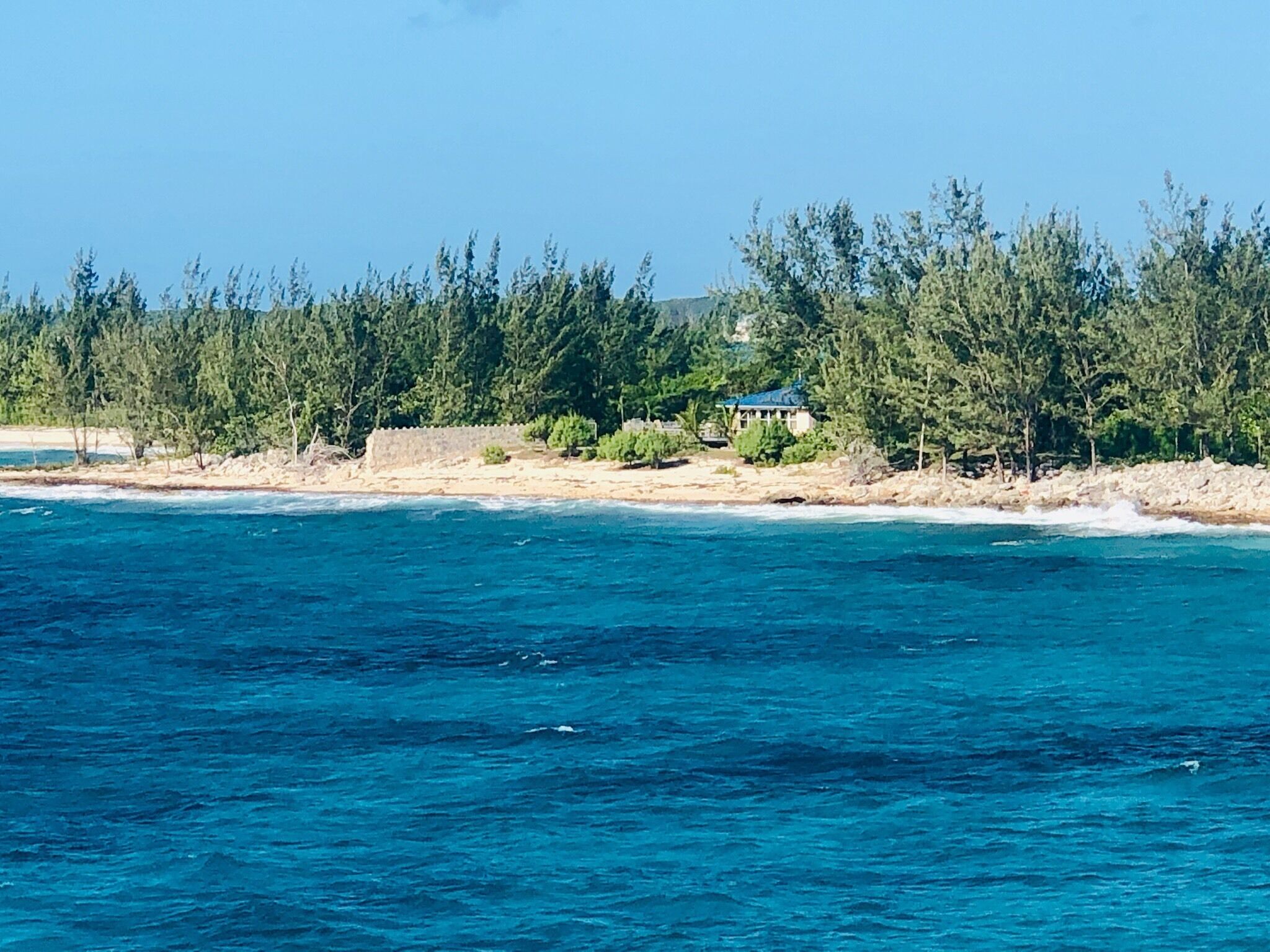 A coastal view with a beach, clear blue water, and a building with a blue roof.