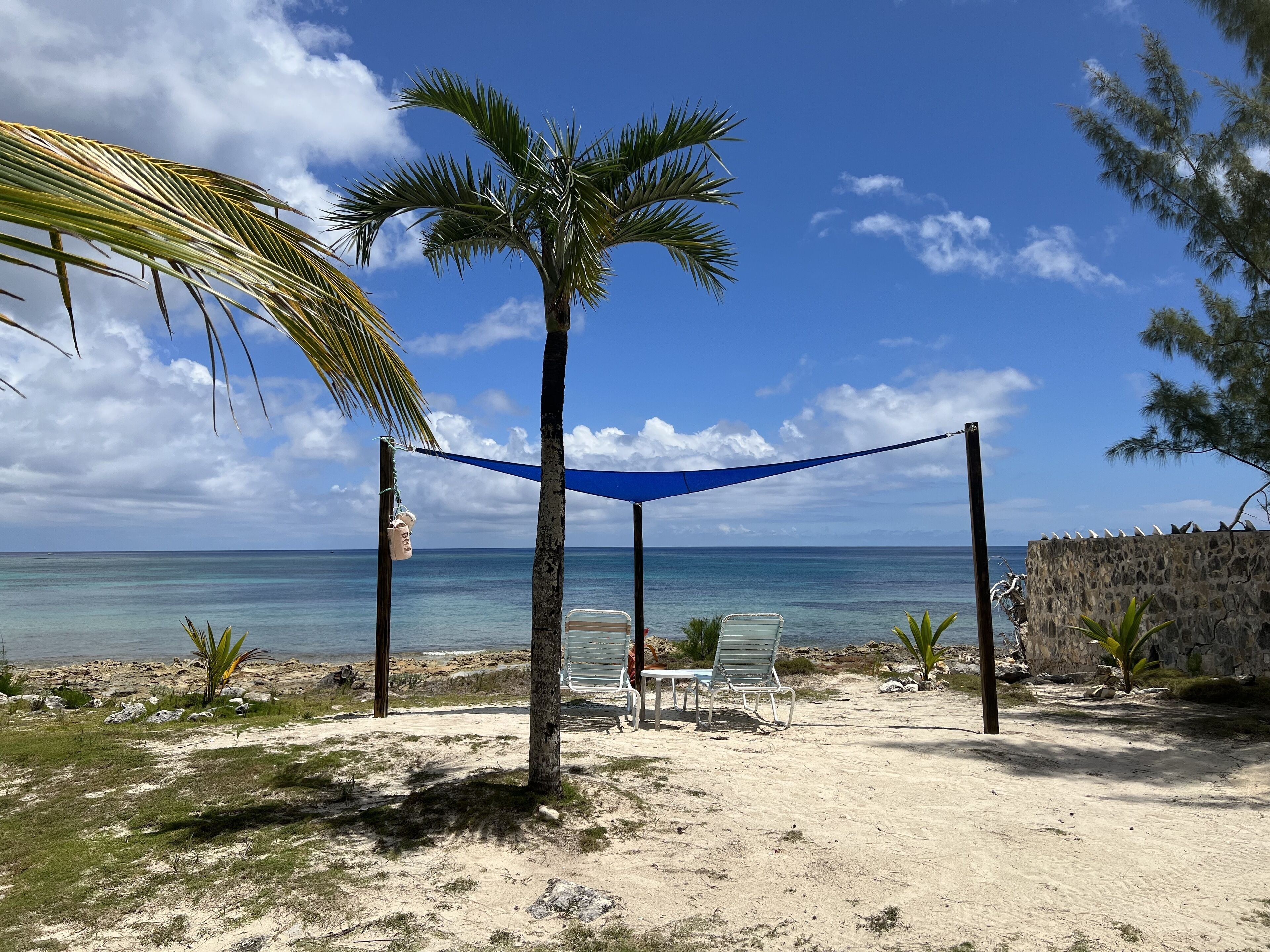 A beach with a hammock, two chairs, a small table, and a thatched structure.