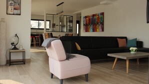 Una sala moderna con un sofá, una mesa de centro y una silla. En el fondo, se aprecia un comedor con una mesa y sillas.