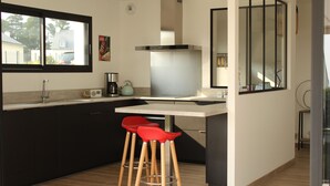 Una cocina moderna con gabinetes oscuros, una encimera blanca, una campana extractora de acero inoxidable y dos taburetes rojos.