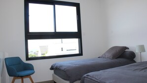 Un dormitorio con dos camas, una ventana, una silla y una lámpara.