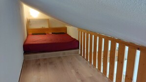 A small, narrow room with a wooden floor, a red bed, and a wooden railing. - studio at the foot of the slopes, view of the mountains, sleeps 5, quiet residence (Les Deux-Alpes)